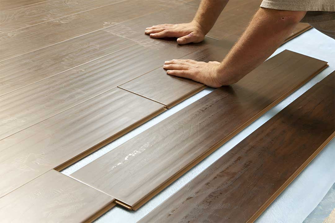 Worker installing SPC flooring using a rubber mallet and spacers to maintain expansion gaps